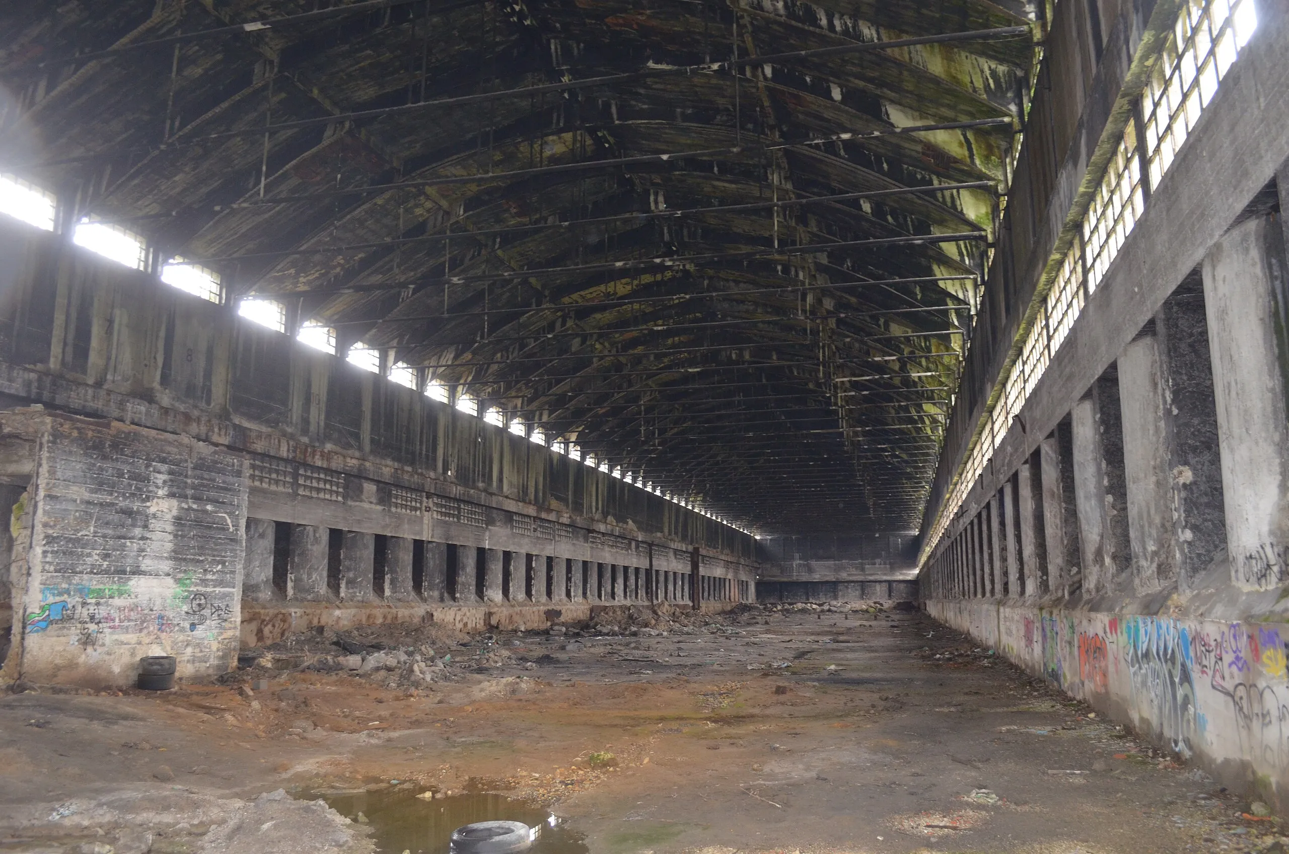 Current interior of an abandoned Nitrastur industrial building with a concrete structure and deteriorated roof.