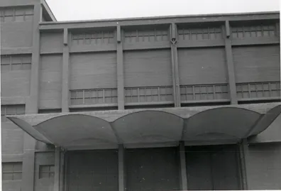 Historic façade of a Nitrastur industrial building with a wave-shaped concrete canopy above the loading bays.