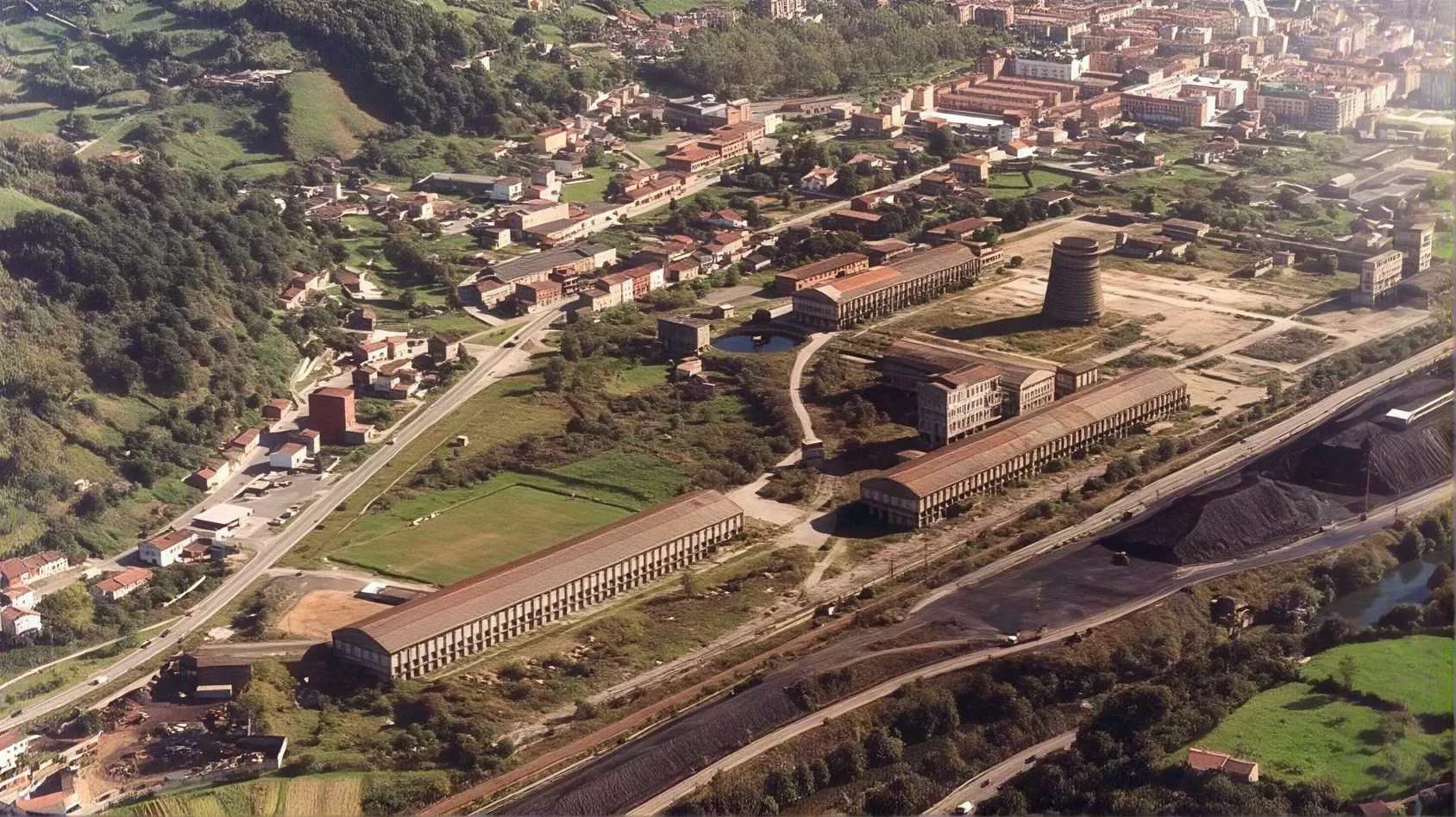 Historic aerial view of the former Nitrastur industrial facilities with a cooling tower and surrounding urban area.