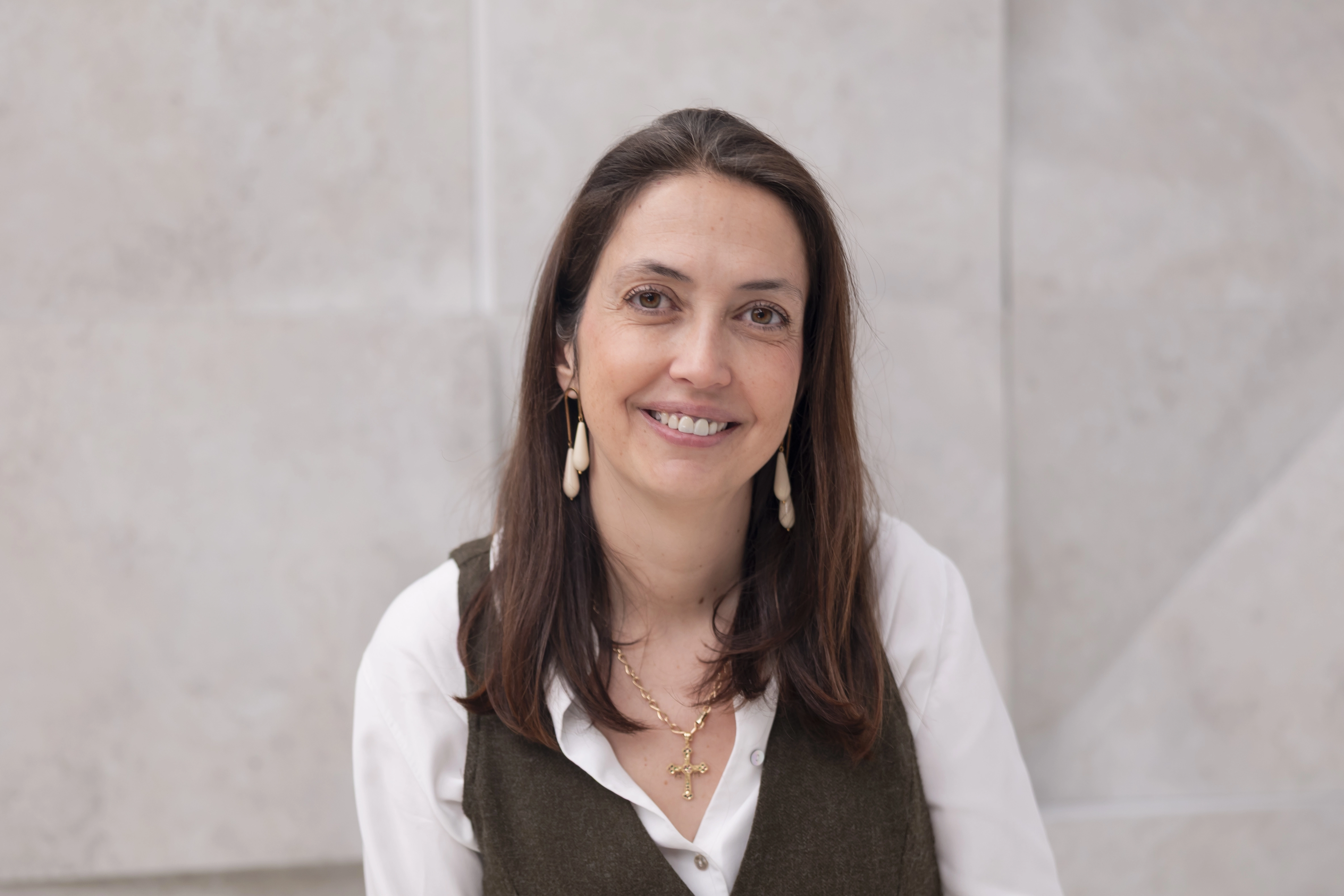 Una mujer sonríe frente a un fondo verde, mostrando una expresión amigable. Tiene el cabello castaño y corto, y lleva un suéter color mostaza. La imagen tiene un estilo gráfico minimalista con un fondo sólido que resalta su rostro.